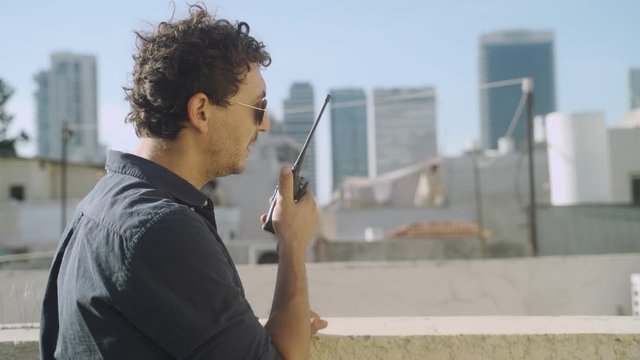 Special agent or spy stands in balcony or city building talking to a radio