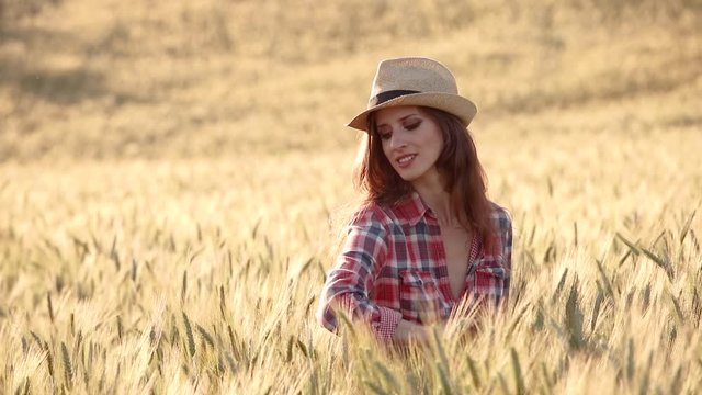 A young woman is touching the grass in a wheat field