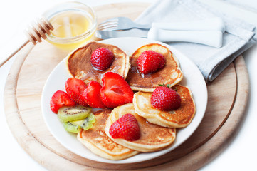 Breakfast with pancakes with strawberry, kiwi and honey on white background. Tasty breakfast for child on wooden board