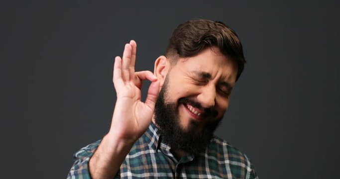 Close up portrait of handsome happy Caucasian man in good mood gestures OK and smiles to camera. Cheerful satisfied male with beard posing indoor with smile on face. Emotions concept