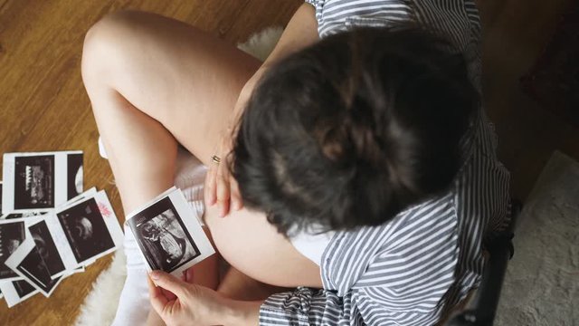 Pregnant woman sitting on floor watching pregnancy ultrasound prints