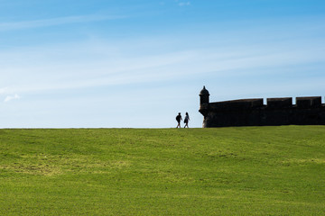 Fototapeta premium Tourists Cross a Field to a Castle in San Juan.