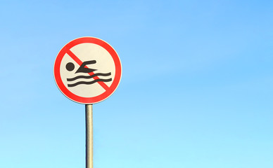 A round sign forbidding swimming in a pond against a blue sky. Selective focus. Forbidding sign: swimming is prohibited. Space for text. Copy space