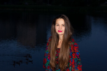 gypsy  young caucasian Ukrainian woman with a long hair at night near the river with red lipstick and in red dress