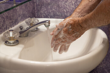 Rubbing hands with soap running water in bathroom sink
