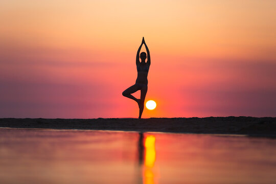 Vrikshasana tree pose from yoga by woman silhouette on sunset