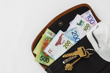 Woman's open wallet with money sticking out of it, keys and mouth mask.
