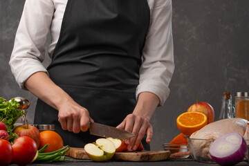 Professional chef cuts apples, fruits for cooking chicken in the oven or grill. Against the background of vegetables, a gray plate for design. Studio light, advertising photo