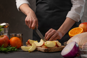 Chef cuts vegetables and fruits, apples for cooking. Against the background of a gray wall. Delicious and culinary recipes.