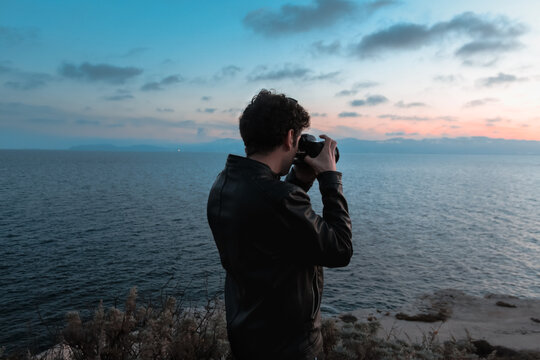 Young and curly photographer taking landscape picture of Calamosca hill at sunset