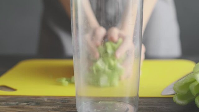 a woman prepares slices on a cutting board ingredients for a celery smoothie and puts them in a blender bowl