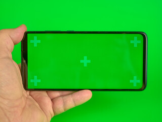 Man's hand holding a mobile phone with a horizontal green screen, chroma key smartphone technology