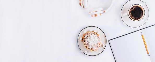 Flat lay of Belgian waffles with marshmallows and coffee, headphones and empty notebook on white background. Top view. Minimal concept