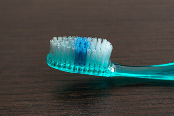 Closeup to a blue thooth brush with white tufts and blue head over a dark brown wooden table. 