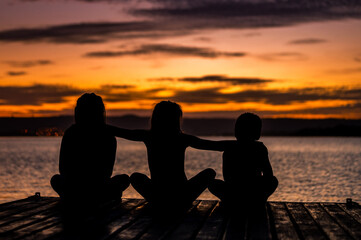 Fototapeta na wymiar children at sunset in front of the lake on the wooden deck