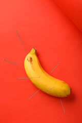 Banana with acupuncture needle  on red background
