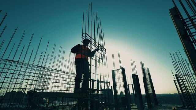 Construction worker knits bars on carcass on a sunset background.