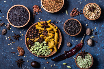 Dry whole warming Indian spices in wooden bowls on dark blue concrete background.