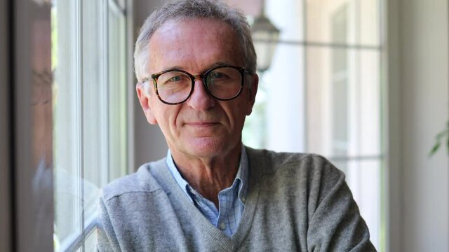 Relaxed mature man at home standing by the window
