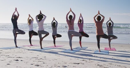 Multi-ethnic group of women doing yoga position on the beach and blue sky background