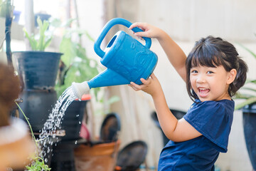 Asian kid girl 6 years old watering water the plant in the garden outside.Stay home plant growing learning activity and child responsibility.Happy asian girl watering garden in morning.Home school. © MIA Studio