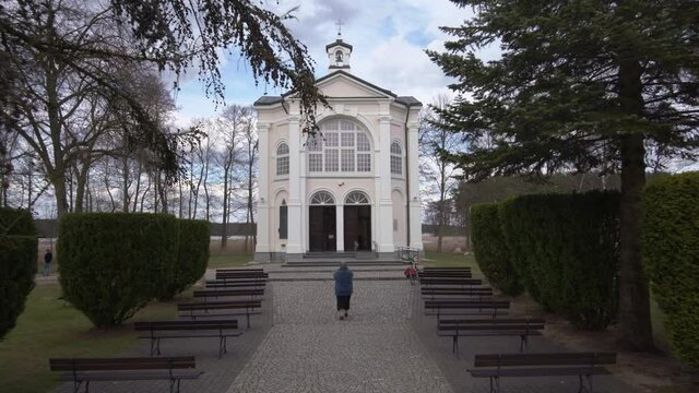 Woman taking picture of chapel, approach wide shot, Suwalszczyzna, Poland