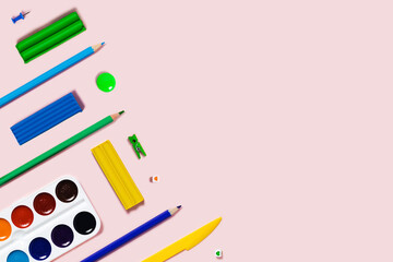 Pink background with writing materials. Back to school flat lay with colored pencils, watercolor, plasticine, and paper clips.