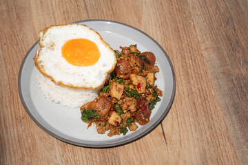 Closed up Famous Thai food padkaprow.  A plate of delicious Stir fried  fresh holy basil mix pork minced and sausage with toped rice fried egg on wooden background.