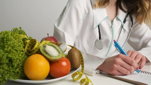 Female doctor nutritionist in a medical gown sits at work and prescribes a healthy diet