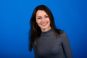 Photo of smiling, cheerful young female in grey dress on blue background