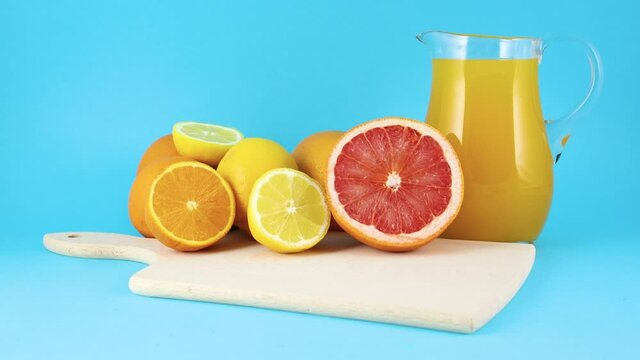 Fresh sliced citrus fruits and jug with fresh squeezed juice on blue background 