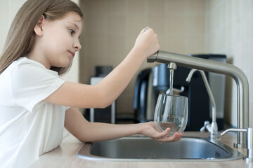 Child is holding a glass under stream of clear transparent cold water from a tap. Close up shot of a young girl pouring a glass of fresh water from a kitchen faucet. Healthy nutrition. World Water Day