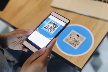 Close up woman hands holding smart phone scanning QR code on the table.