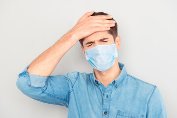 Portrait of ill sick young man in blue shirt wear medical safety face mask, touching his head feeling pain influenza respiratory disease symptom temperature cold, corona virus pandemic 2020 concept