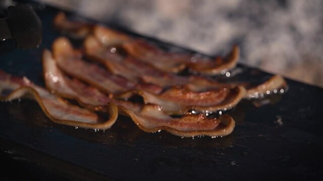 Cooking bacon in grease on a cast iron pan over an open campfire flame outside