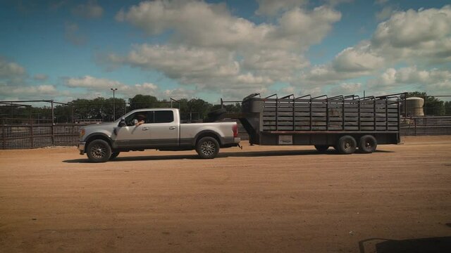 Gray truck towing a trailer driving by cow pens on cattle farm in slow motion