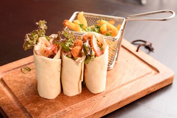 wrap de pollo  encima de  una tabla de picar de madera  mas un poco de guarnición en una...