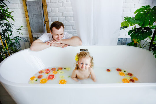 Cute little girl sitting in a bath with milk and fruit. in summer. A young family spends time together. The concept of a family holiday.