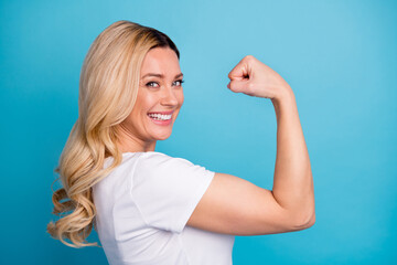 Closeup profile photo of attractive lady wavy blond hairdo raise arm showing big shape muscle biceps successful sporty person wear casual white s-shirt isolated blue color background - obrazy, fototapety, plakaty