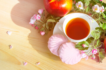 On a wooden background, a branch of apple flowers, a mug with tea, marshmallows and red apples. Still life. Close-up, food and spring concept, postcard. Copy space, place for text.