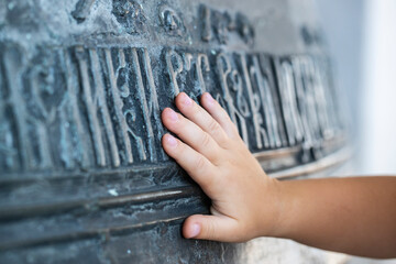 Close-up. The hand of the child touches a large church bell with ancient Slavic inscriptions. The...