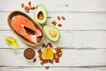 Food high in omega-3 fatty acids on a white wooden background. Healthy eating concept. Salmon, avocado, flax seeds, fish fat capsules, oil, almonds. Top view, flat lay. - obrazy, fototapety, plakaty