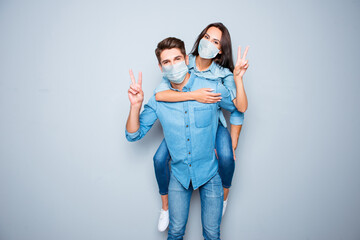 Smiling happy boyfriend carry piggy back his girlfriend gesturing v-sign wear medical safety...