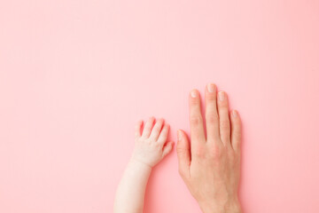 Hands of young mother and infant on light pink table background. Pastel color. Closeup. Copy space....