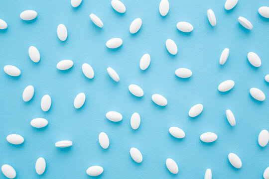 White pills on light blue table background. Pastel color. Drugs pattern. Medical, pharmacy and healthcare concept. Closeup. Top down view.