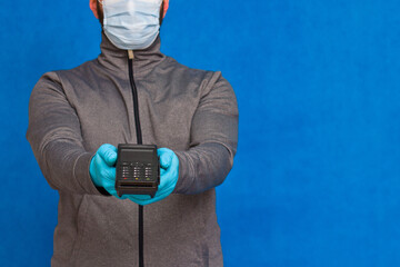 A man holding a wireless POS terminal to pay by credit card. In rubber gloves and face mask. Isolated on blue background.