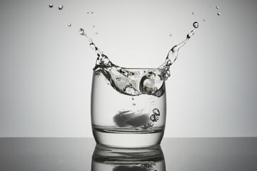 Ice falls into a glass of water with splashes, drops and air bubbles.