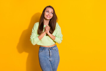 Photo of attractive pretty funny lady good mood hold arms together look side empty space overjoyed wear green cropped sweatshirt jeans isolated vivid bright yellow color background