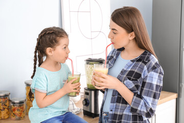 Mother and little daughter with healthy smoothies in kitchen