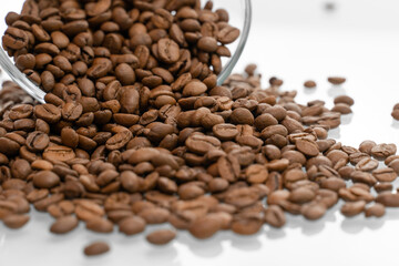 Coffee beans pour out of a glass bowl onto a light surface. coffee background